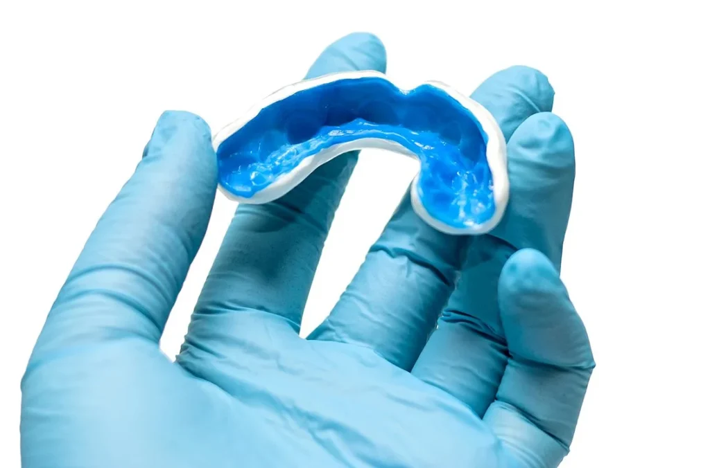 Photo of gloved dental assistant holding a mouth guard in its mold
